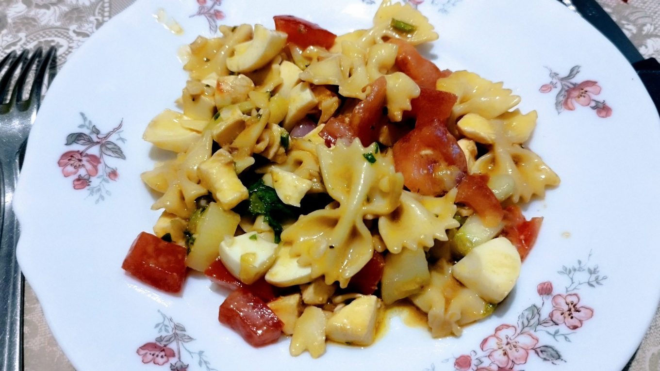 Salade de pâtes estivale avec farfalle, tomates, mozzarella et œufs, assaisonnée à l’huile d’olive.