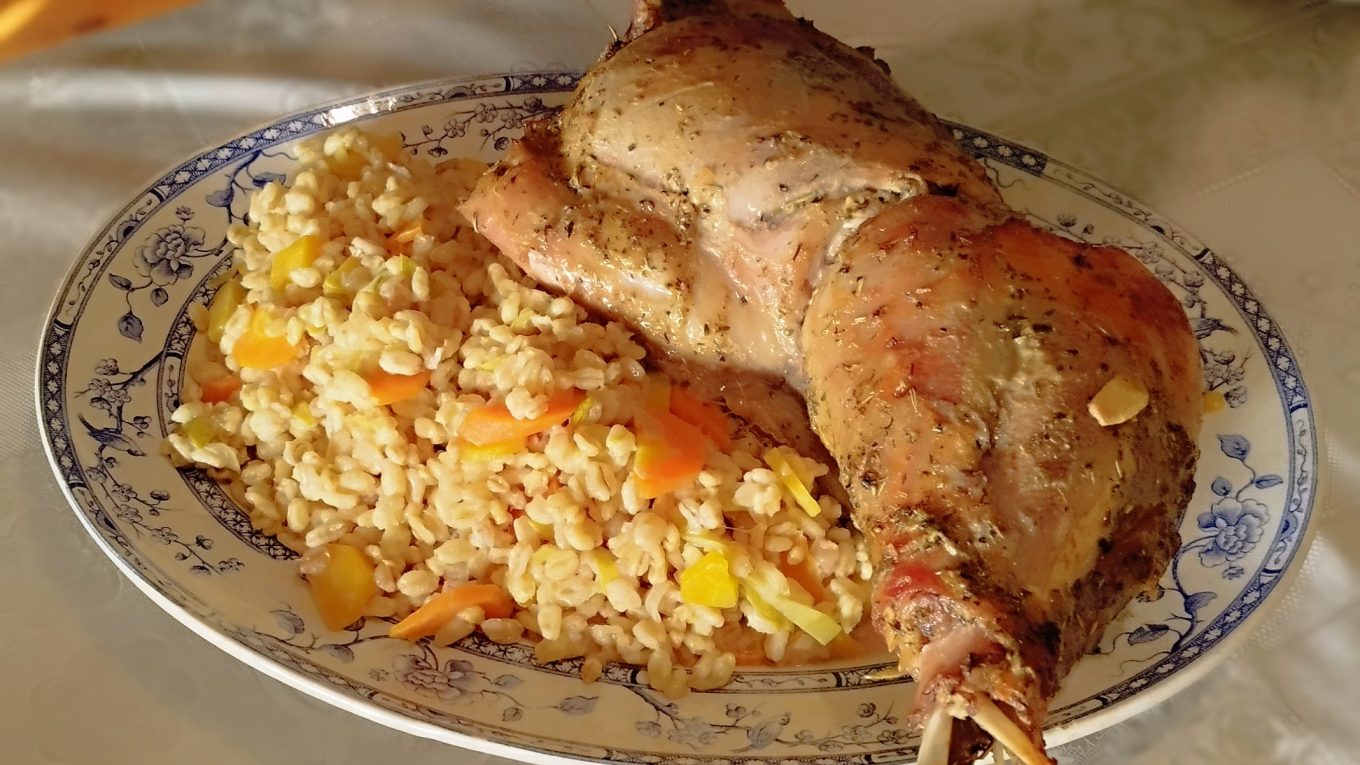 Cuisse de dinde rôtie aux herbes servie dans un plat ovale avec un accompagnement d’orge perlé et de légumes.