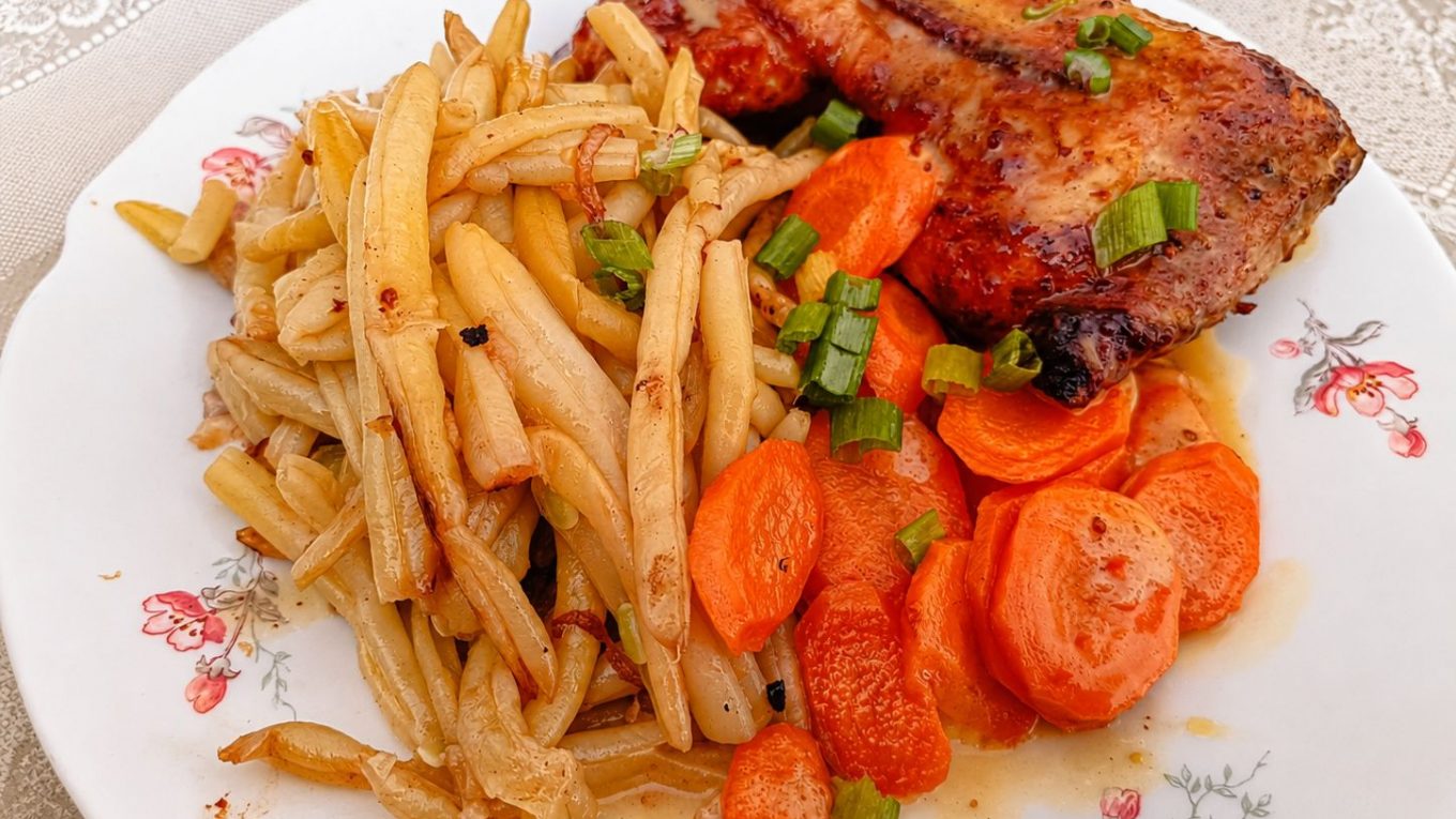 Cuisse de poulet rôtie au miel, servie avec des haricots beurre poêlés et des carottes fondantes.